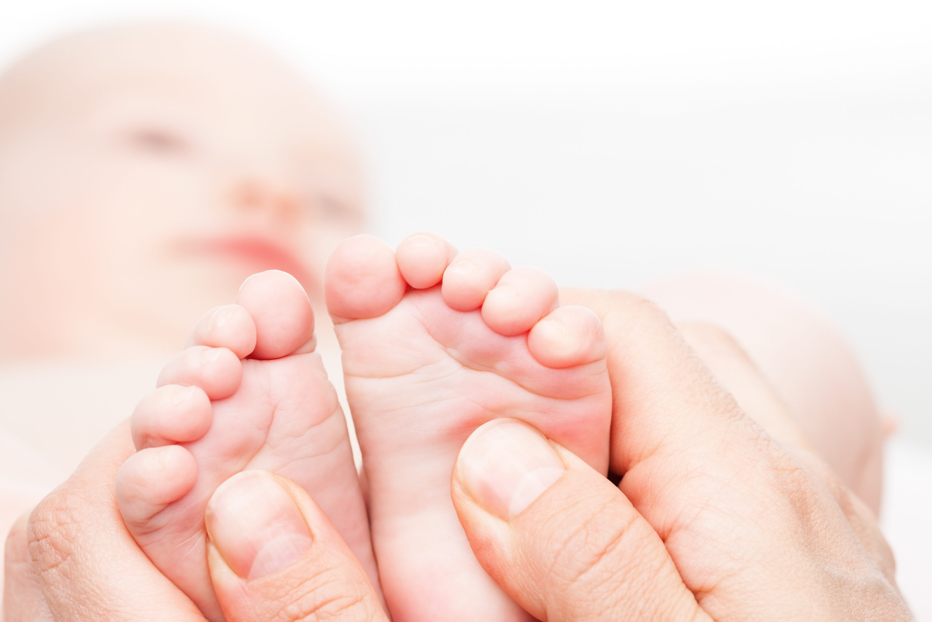 Close-up shot of three month baby girl's foot manipulated by osteopathic manual therapist or physician